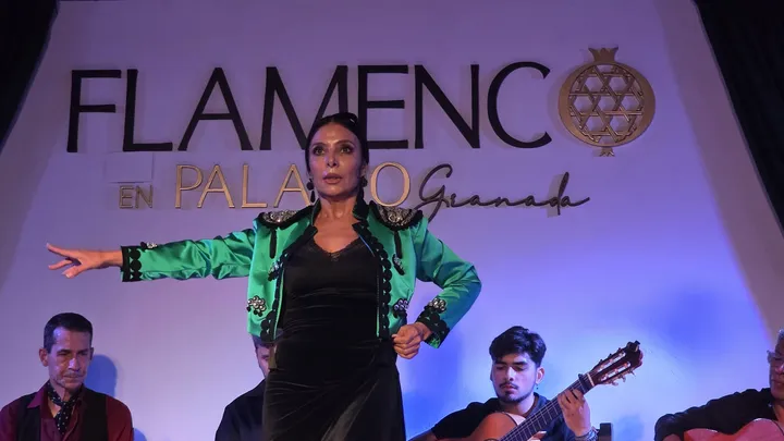 Bailaora con chaquetilla verde y el brazo extendido ante el cartel del tablao, con el cantaor y el guitarrista sentados detrás