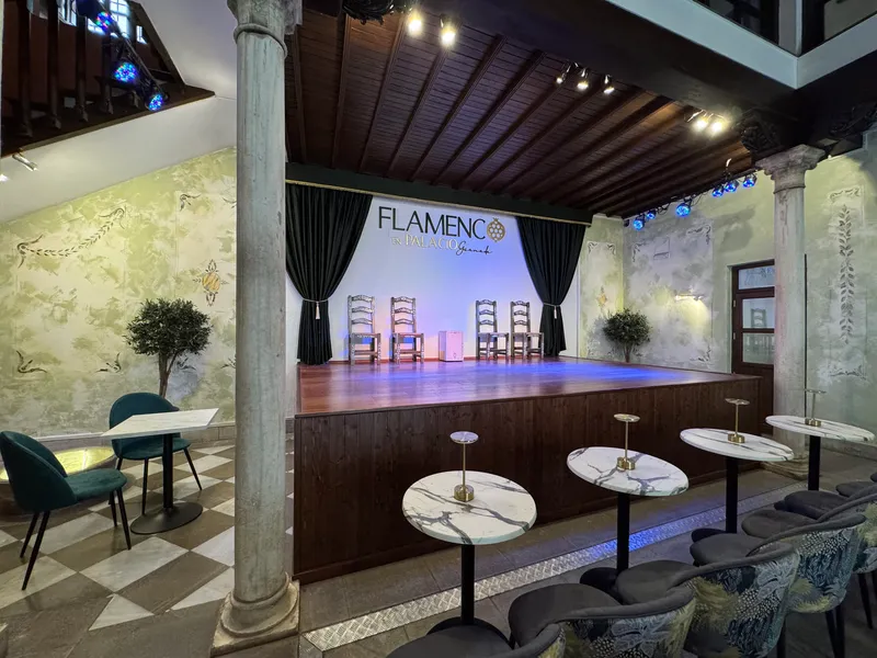 Sala del tablao vacía vista en diagonal, con el escenario y sus cuatro sillas de enea, las columnas de mármol y el suelo ajedrezado