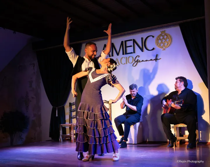 Bailaora arqueada hacia atrás con traje de volantes y un bailaor con los brazos en alto detrás, con el palmero y el guitarrista al fondo